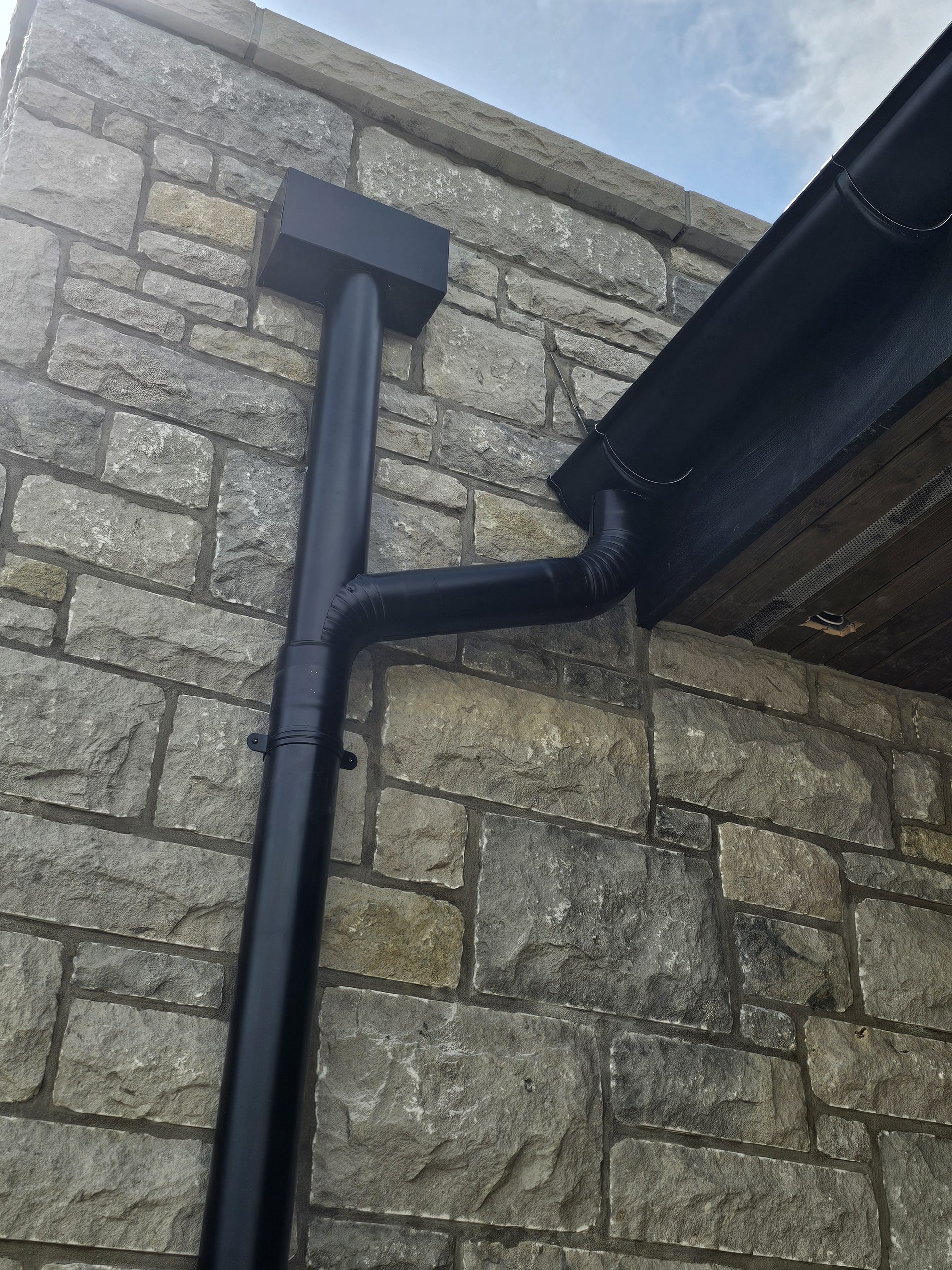 Dark eavestrough detail on a stone-clad exterior